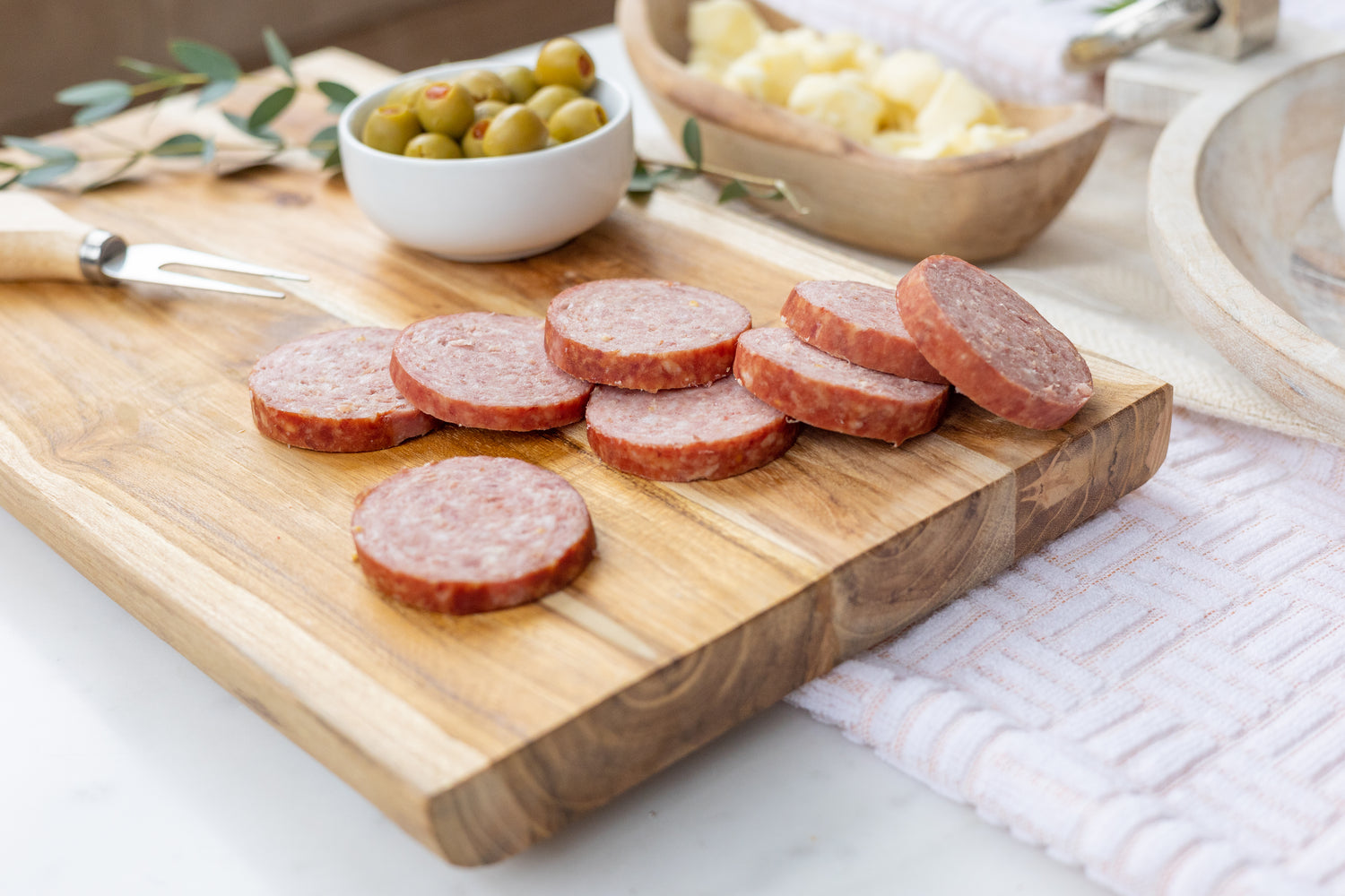 3 logs of summer sausage on a white cutting board